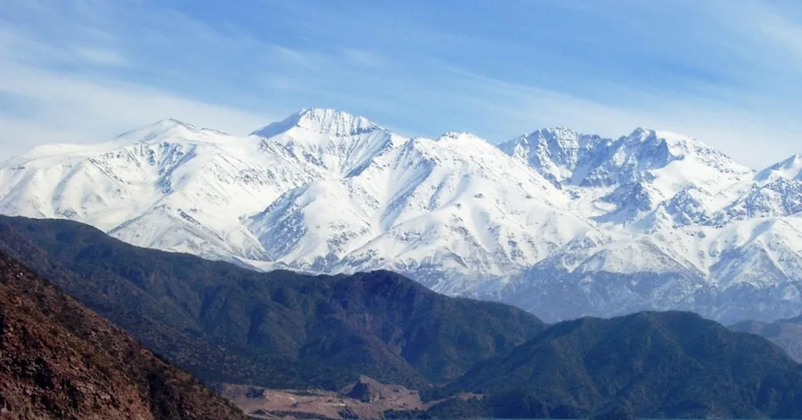 The huge snow-covered south face of Aconcagua above dark foothills under a blue sky